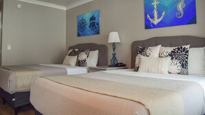 A hotel room with two beds, a nightstand, a lamp, and nautical-themed artwork on the walls.