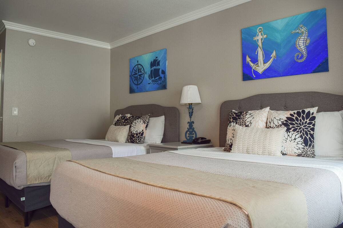 Ein Hotelzimmer mit zwei Betten, einem Nachttisch, einer Lampe und maritimer Kunst an den Wänden.