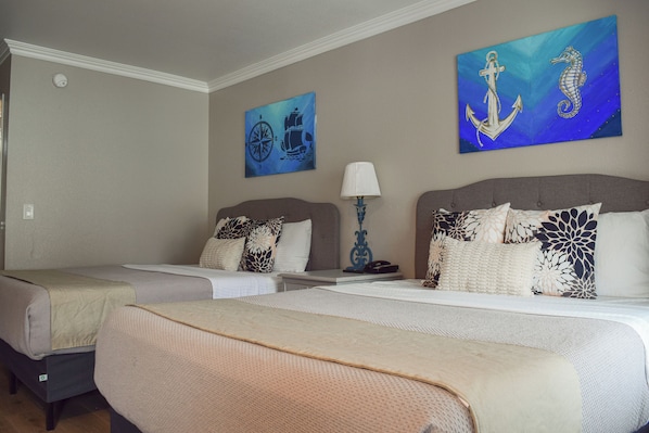 A hotel room with two beds, a nightstand, a lamp, and nautical-themed artwork on the walls.