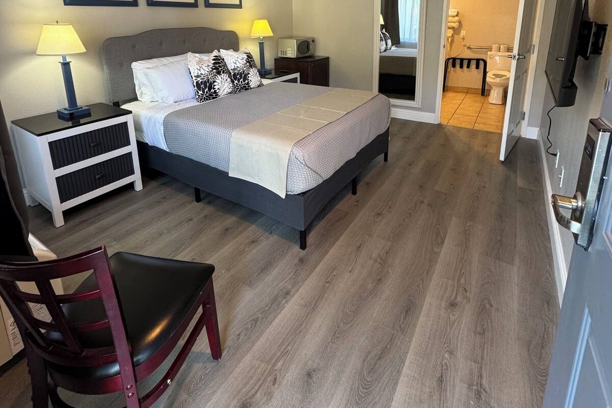 Ein Schlafzimmer mit Bett, Nachttischen, einem Sessel, einem Fernseher und einem durchgehenden Tür sichtbaren Badezimmer.