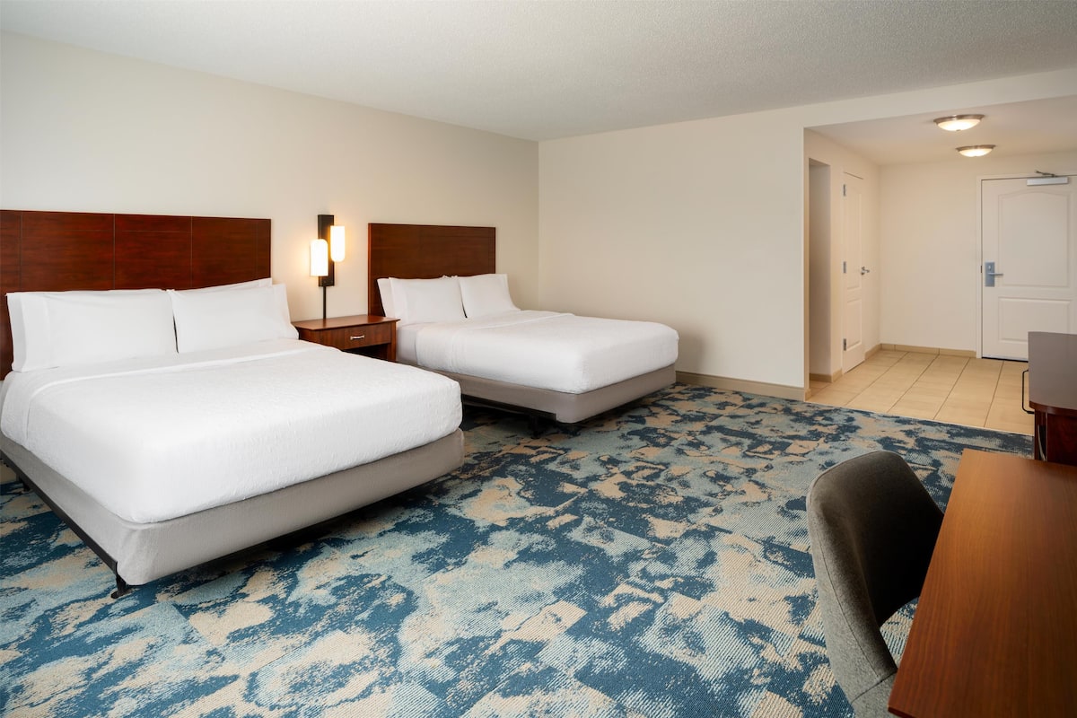 A hotel room with two beds, a desk, and a chair.