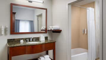 Un baño con lavamanos de encimera de granito, un espejo, toallero y zona de ducha con cortina.