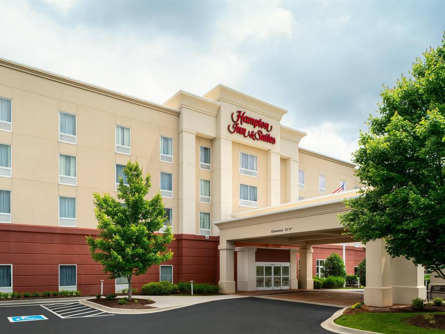 A Hampton Inn & Suites hotel with a beige facade, a clear sky, and a parking lot with handicap spaces.