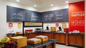 Zona de desayuno tipo buffet con diversas opciones de comida y un cartel que promociona waffles.