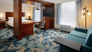Habitación de hotel con una cama grande, un escritorio, una silla, un televisor, un sofá y una ventana con cortinas.