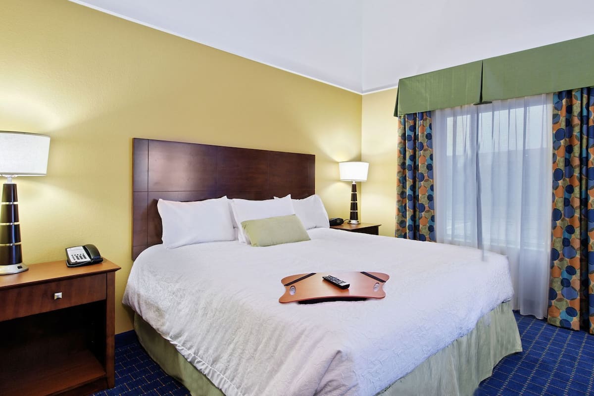A hotel room with a bed, bedside tables, a telephone, a remote control, and curtains.