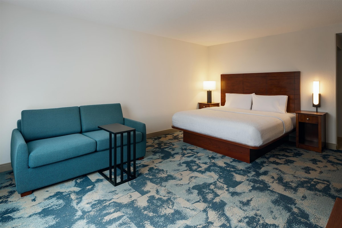 A hotel room with a bed, a blue sofa, a small table, and two bedside lamps.