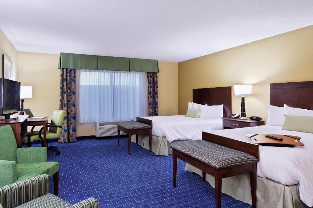 A hotel room with two beds, a desk, a chair, and a bench.