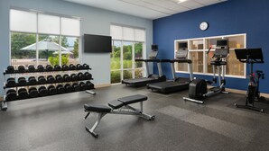 Un gimnasio con cintas de correr, una banca, mancuernas y una pantalla de televisión.