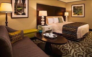 Una habitación de hotel con cama, mesitas de noche, una mesa de centro, sofá y una alfombra estampada.