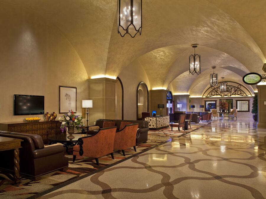 A spacious lobby with a high ceiling, comfortable seating, a reception desk, and a television.