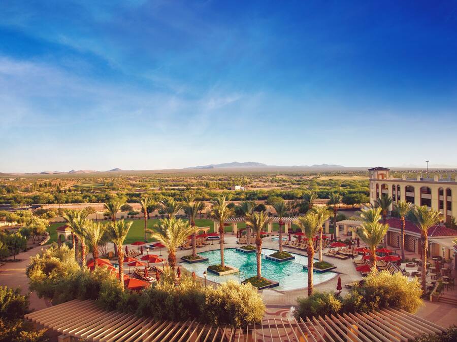 Un resort con piscina central, palmeras y vistas a montañas distantes.
