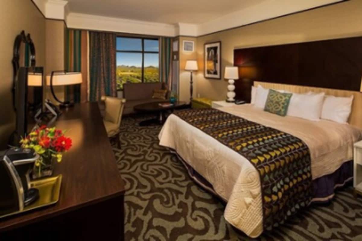 A hotel room with a large bed, a desk with a lamp, a chair, and a view of a landscape through the window.