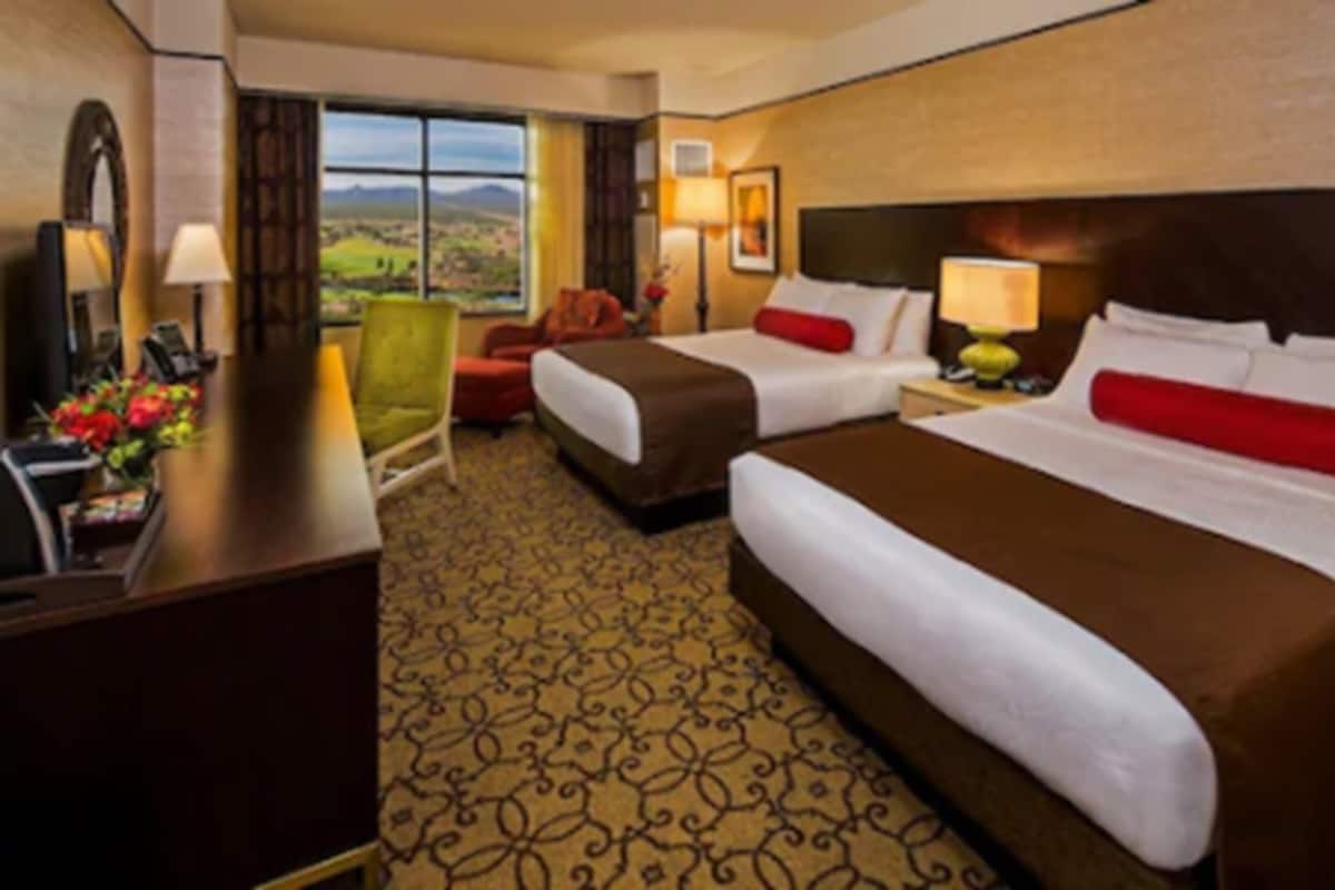 A hotel room with two beds, a desk, a chair, and a view of the countryside.