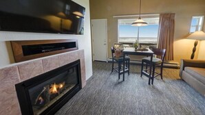 Una sala de estar con chimenea, un televisor de pantalla plana montado encima, una zona de comedor con mesa y sillas, y un ventanal con vistas al océano.