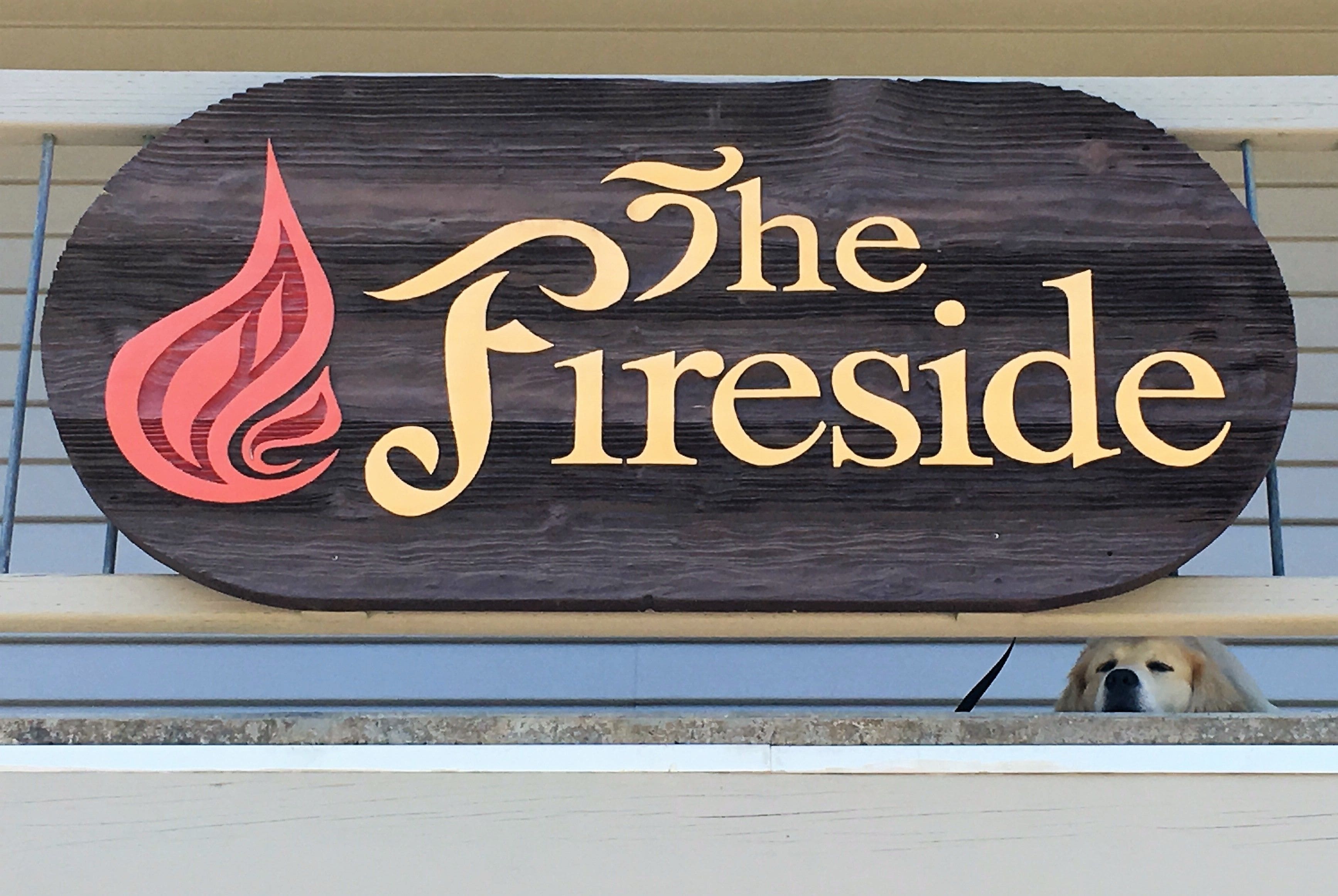 Un cartello di legno con il testo "The Fireside" e un disegno stilizzato di una fiamma.