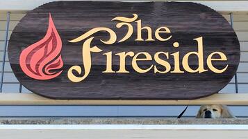 Un cartello di legno con il testo "The Fireside" e un disegno stilizzato di una fiamma.