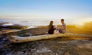 Two people sitting on a log by the ocean during sunset.