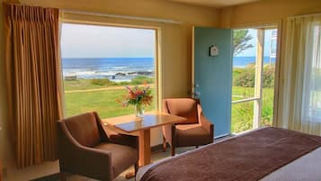 A hotel room with a bed, two chairs, a table, and a view of the ocean.