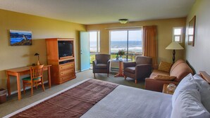 Habitación de hotel con una cama grande, un escritorio con silla, televisor, dos sillones, un sofá y un balcón con vista al océano.