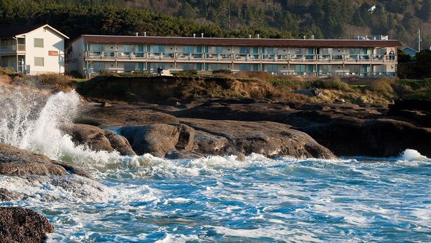 Un hotel costero con una estructura alargada, múltiples balcones y vistas a la accidentada costa rocosa.