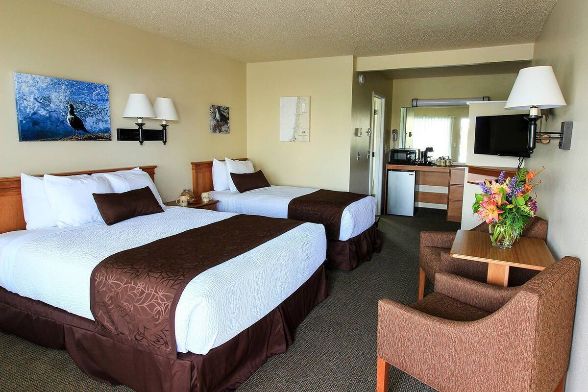 A hotel room with two beds, a desk, a chair, a television, and a small kitchenette.
