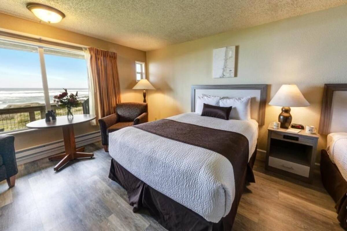A hotel room with a large bed, two bedside tables, a chair, a small table, and a view of the ocean.