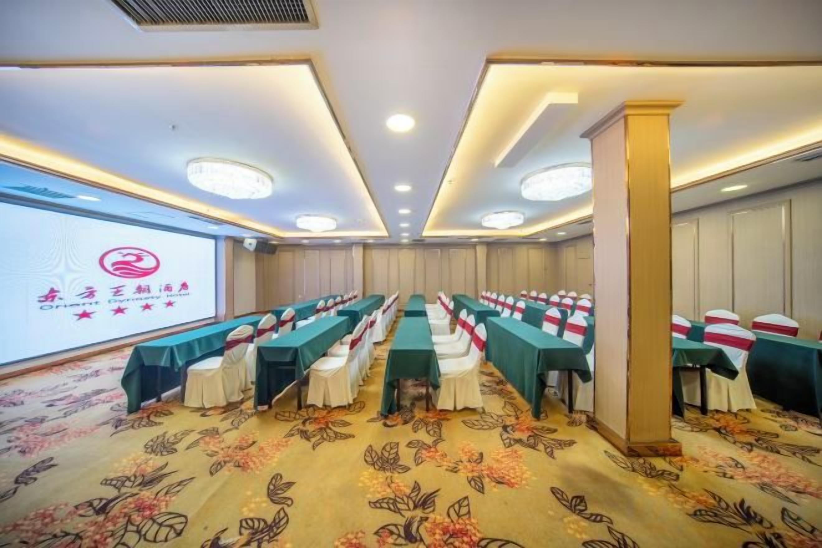 A conference room with rows of tables and chairs, a projector screen, and a carpeted floor.