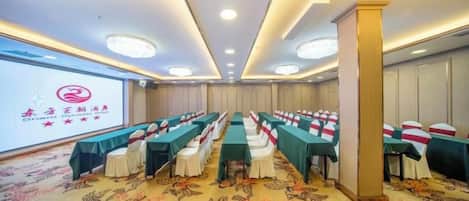 A conference room with rows of tables and chairs, a projector screen, and a carpeted floor.