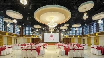 A large hall with rows of tables and chairs, a stage with a screen, and chandeliers.