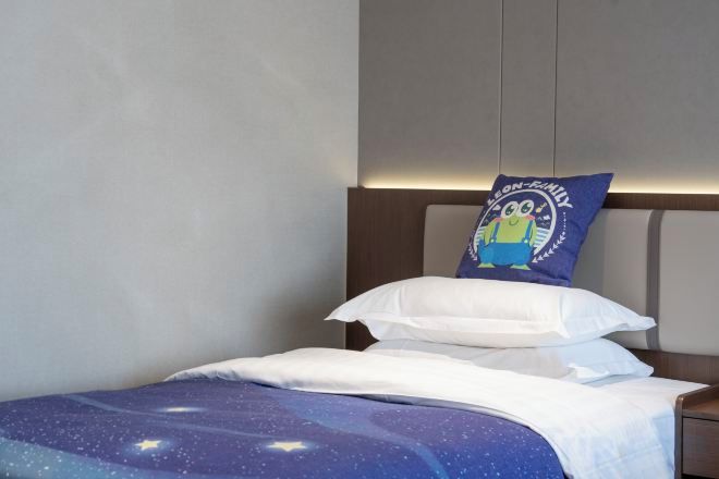 A neatly made bed with a galaxy-themed bedspread, a pillow with a cartoon character, and a headboard with built-in lighting.