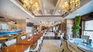 Ein Hotelrestaurant mit mehreren Tischen und Stühlen, einer Kronleuchterbeleuchtung und einem Fernsehbildschirm.