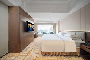 Habitación de hotel con una cama grande, un televisor montado en la pared, un escritorio con una lámpara y vistas a la ciudad desde la ventana.