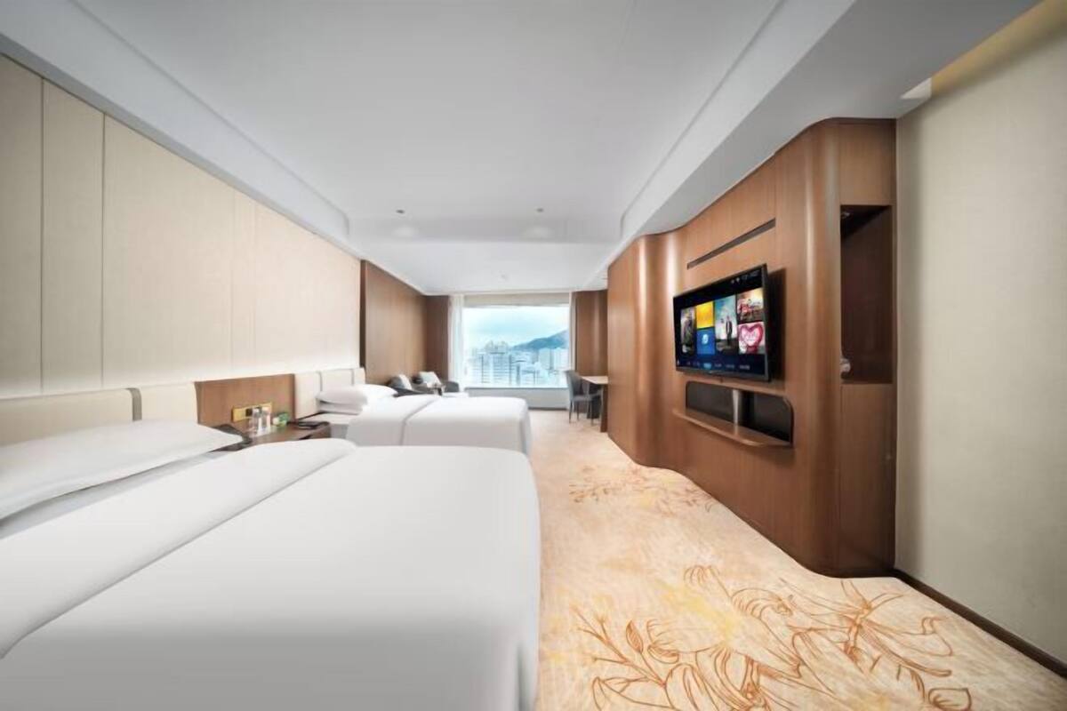 A hotel room with two beds, a TV, a desk, and a view of the city.