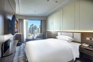 Habitación de hotel con una cama grande, televisión, escritorio con teléfono y vistas a la ciudad.