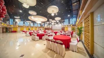 A spacious hall with multiple round tables, each with a red tablecloth and white chairs, arranged for a gathering.
