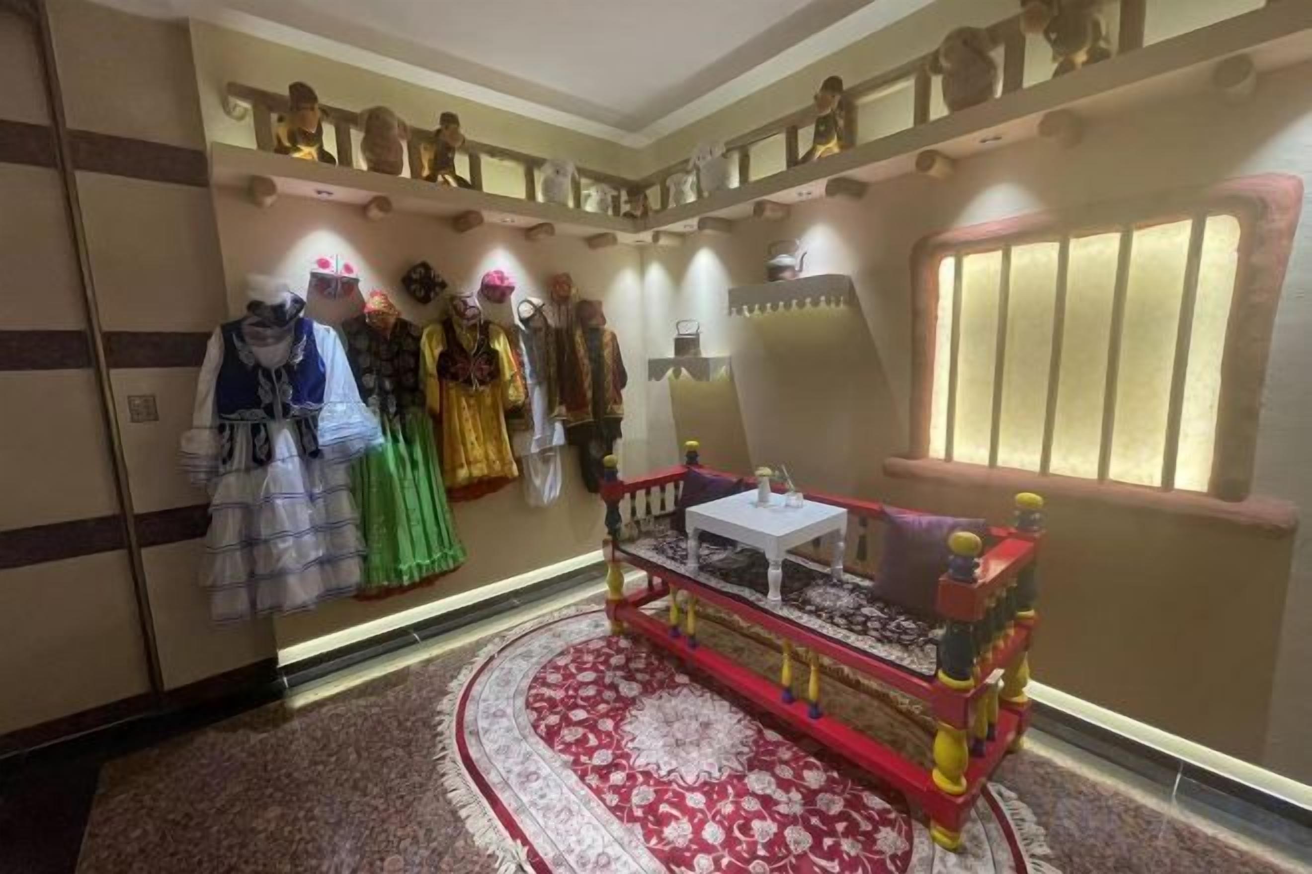 Een kamer met een rijk versierde rode en gouden bank, een rood tapijt en een muur met mannequins waarop verschillende outfits gepresenteerd worden.