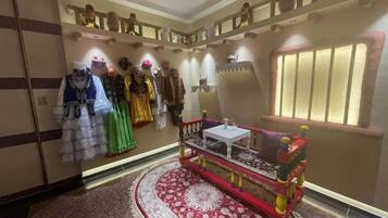 Een kamer met een rijk versierde rode en gouden bank, een rood tapijt en een muur met mannequins waarop verschillende outfits gepresenteerd worden.
