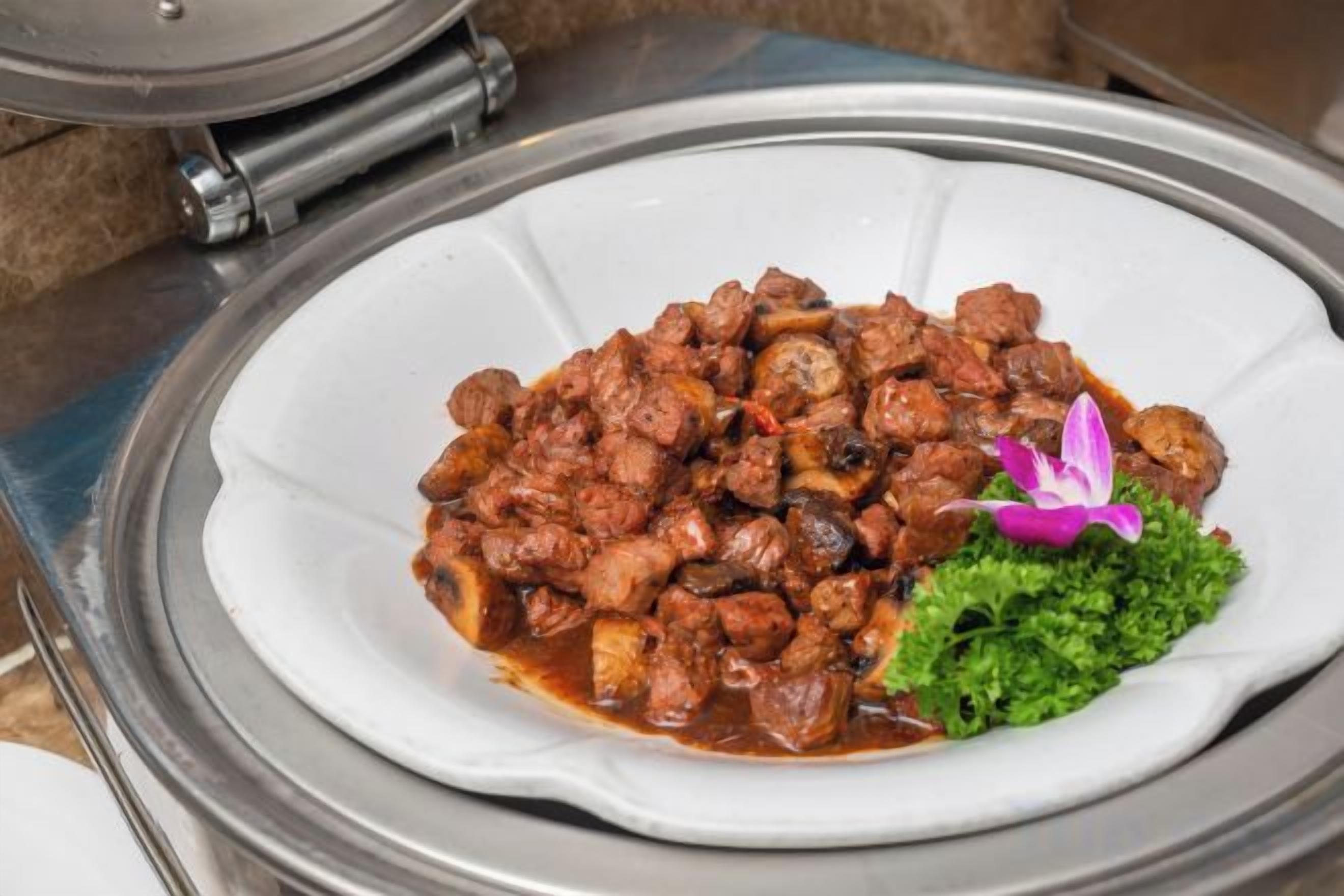 A white plate with a meat dish, garnished with a purple flower, on a table.