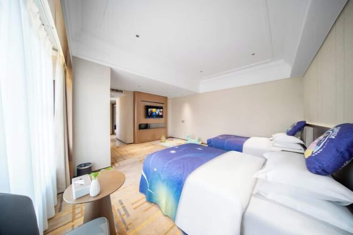 A hotel room with two beds, a TV, a small table, and a window with curtains.