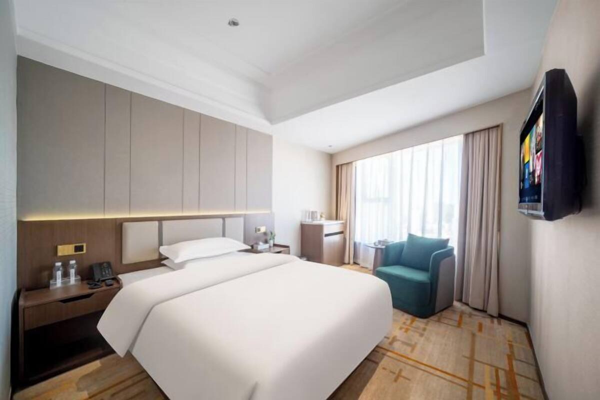 A hotel room with a large bed, a desk with a lamp, a chair, and a TV mounted on the wall.