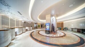 Eine moderne Lobby mit einer zentralen Rezeption, einem großen Bildschirm und einer runden Sitzecke.