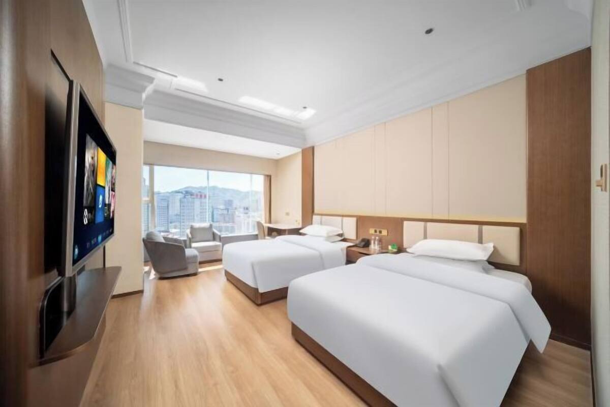 A hotel room with two beds, a TV, a desk, and a chair.
