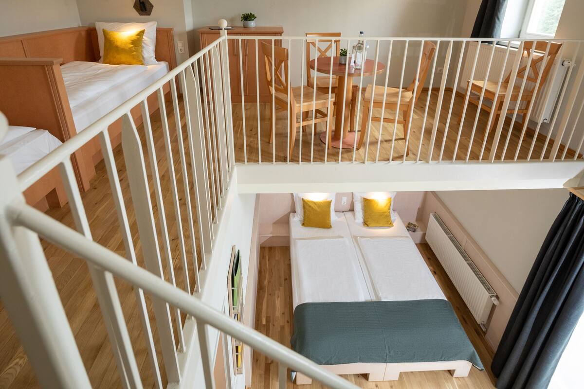 A multi-level room with a bunk bed, a desk with a chair, and a dining table with chairs.
