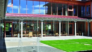 Un edificio moderno con un patio cubierto, mobiliario exterior y una fuente de agua.