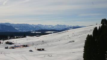 Ein mit Schnee bedeckter Ski-Hang mit Seilbahnen, Gebäuden und Bergen im Hintergrund.