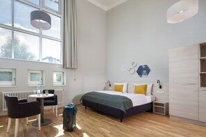 A modern hotel room with a bed, a desk, and a chair. There is a suitcase on the floor. - JUFA Hotel Kempten (Kempten)