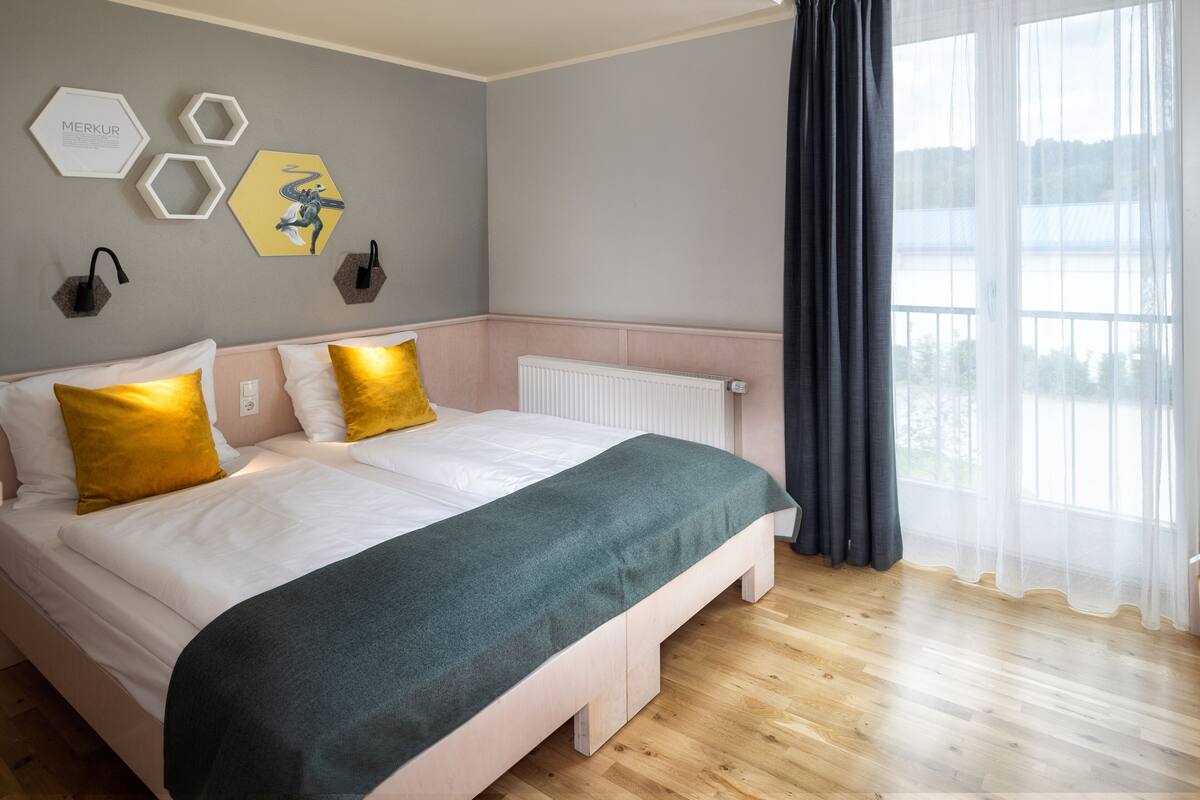 A double bed with white and green bedding, a radiator, and a window with curtains.