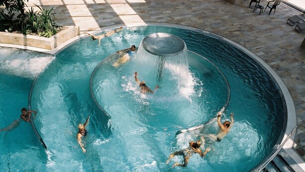 Una piscina circular con una fuente central y personas nadando.