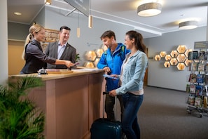 Una mesa de recepción con una recepcionista, un hombre y una mujer de pie frente a ella.